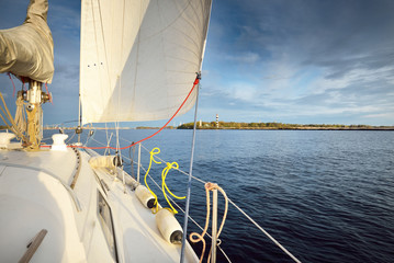 White yacht sailing in the Baltic sea after the rain at sunset. Riga, Latvia. Close-up view from the deck to the bow, mast and sails. Clear blue sky. Sport, recreation, leisure activity, travel