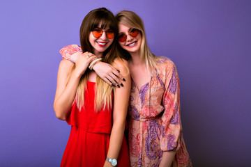 Wall Mural - Friendship and communication concept, two sisters best fronds girls wearing colocar matching trendy summer dresser hugs and looks on camera, boho glasses, purple background.