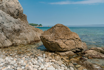 Poster - Rock and large boulder by the sea with a pebble beach in the midday sun