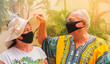 © Vasleriia Kuznetsova - happy retirees wearing masks for safety.  a retired elderly man looks under the old woman's hat to look at his wife.