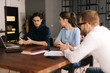 © dikushin - Young business man tells his colleagues about the project in modern office meeting against large panoramic window. Young man and woman listen to the speaker. Concept of office life.