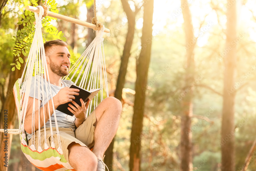 Young man with book relaxing in hammock outdoors