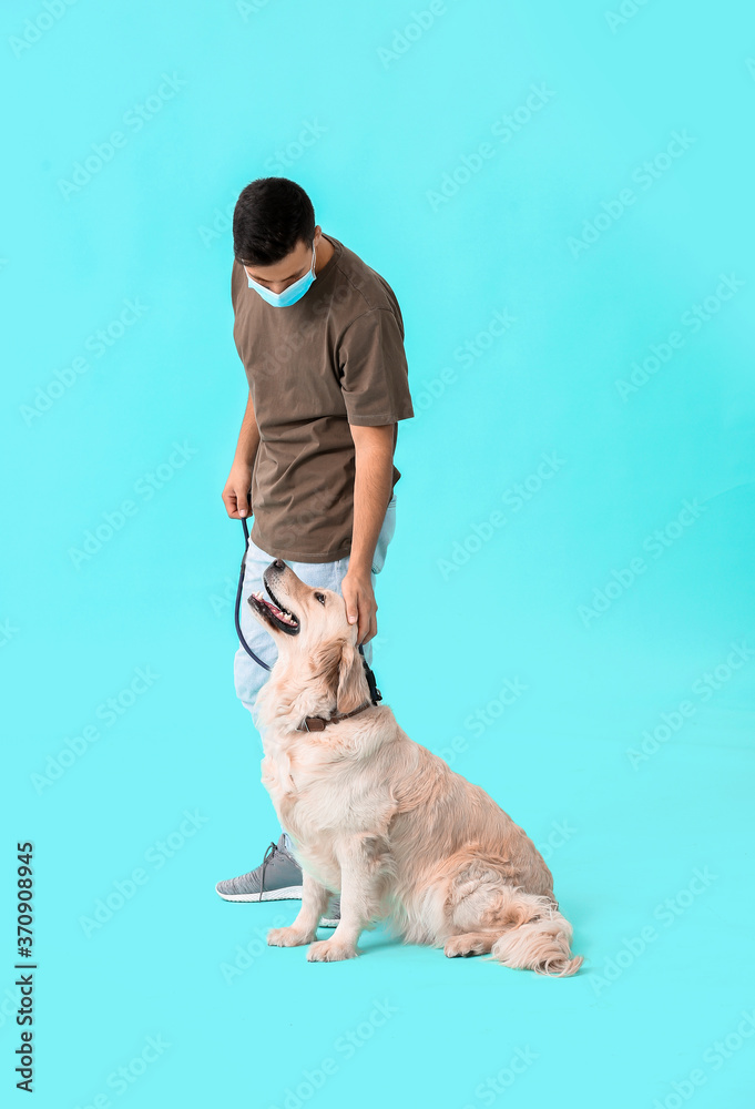 Young man in protective mask and with cute dog on color background