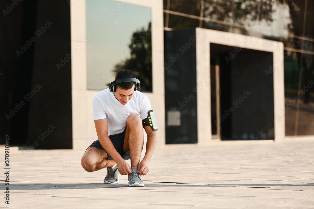 Sporty young man tying shoelaces outdoors