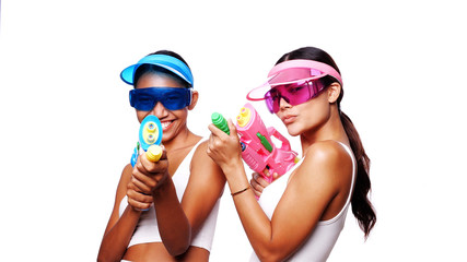 Portrait of two beautiful Asian women in pink and blue sun visor cap and sunglasses posing with water guns over white background