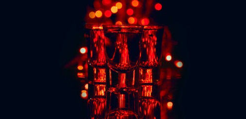 Poster - Red alcohol cocktails in shot glasses over red bokeh light and black background. Shots on bar counter in night club party.