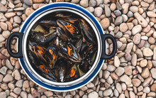 Boiled Mussels With Garlic And Herbs In Cooking Pot On The Sea Pebbles Background