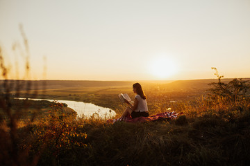 Calm girl reading a book on hill with perfect landscape, enjoying time on holiday. She read book in quiet nature.