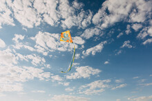 Colorful Kite Flying On Blue Sky Background With White Clouds.
