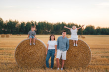 Happy Family Of Four Having Fun And Playing In A Wheat Field In Summer At Sunset Time..