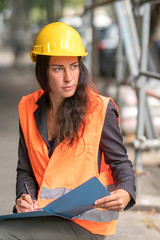 Absorbed female civile engineer wearing safety helmet and vest checking office blueprints 