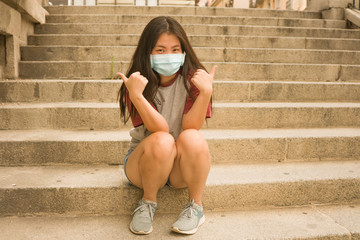 new normal urban portrait - young happy and beautiful Asian Chinese woman in face mask sitting outdoors at city street staircase smiling free after home lockdown