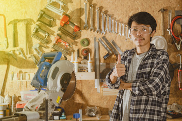 Portrait of asian craftsman with equipment standing in workshop and looking at camera. Carpenter in workplace. Asian man carpenter showing thumb up