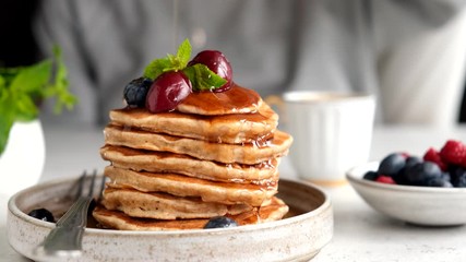 Wall Mural - Pouring syrup on pancakes. Healthy oat pancakes with berries and maple syrup. Breakfast food concept