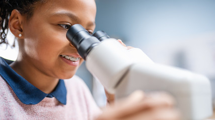 portrait of smart little schoolgirl looking under the microscope. in elementary school classroom cut