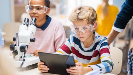 Poster - Elementary School Science Classroom: Boy Uses Digital Tablet Computer to Check Information on the Internet while Enthusiastic Cute Little Girl Uses Microscope.
