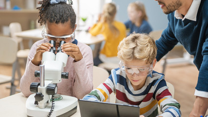 Poster - Elementary School Science Classroom: Cute Little Girl Looks Under Microscope, Boy Uses Digital Tablet Computer to Check Information on the Internet. Teacher Observes from Behind