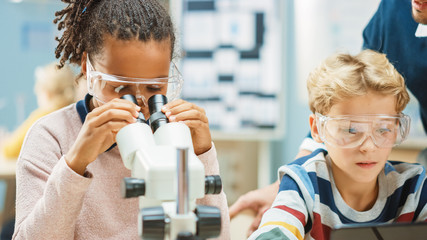 Poster - Elementary School Science Classroom: Cute Little Girl Looks Under Microscope, Boy Uses Digital Tablet Computer to Check Information on the Internet. Teacher Observes from Behind