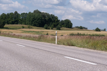 highway meter post behind which opens a great summer day landscape with a wonderful ecological meadow and forest