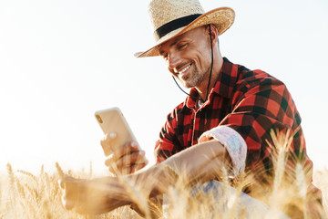 Wall Mural - Image of smiling adult man in straw hat taking photo on cellphone
