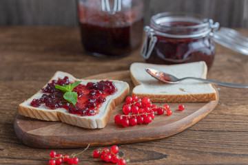 Poster - Homemade red currant jam in a glass jar and a number of berries on a wooden background. Toast or bread with marmalade for breakfast. Preparations for the winter from berries and fruits