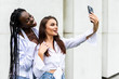 © F8  \ Suport Ukraine - Cheerful young mixed race women taking a selfie outdoors on the street. Two female friends making a self portrait outside in the city.