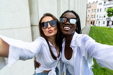 Wall Mural - Cute outdoor portrait of funny pretty best friends girls having fun making selfie at city center, positive crazy emotions, traveling together in Europe, joy, vintage glasses, bright make up.