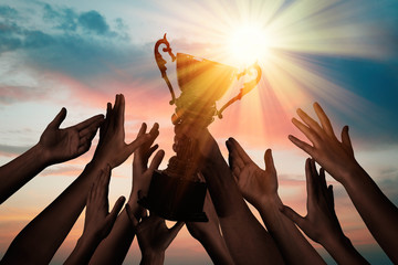 winning team with gold trophy cup against shining sun in sky