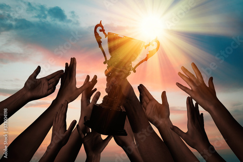 Fotografía Winning team with gold trophy cup against shining sun in sky
