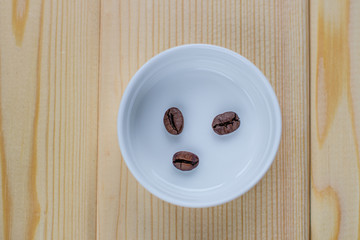 Poster - A few coffee beans in a white Cup on a wooden background.