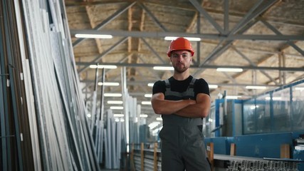Wall Mural - Worker in grey uniform and hard hat stands indoors in the factory with arms crossed.