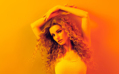 Fashion. Woman in colorful neon gold light, make-up. Beautiful blond girl, stylish curly hair, trendy makeup. Golden neon portrait. Creative beauty, fashionable model face, voluminous hairstyle