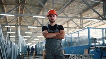 Wall Mural - Worker in grey uniform and hard hat stands indoors in the factory with arms crossed.