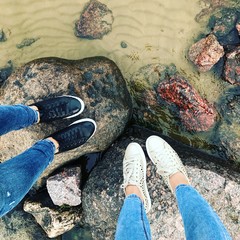 Legs in sneakers and jeans stand on stones in the water. High quality photo