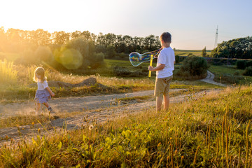 Happy children playing with soap bubbles on a summer nature. Bubbles in the sunset