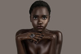A portrait of a serene young black female with short black hair, moist lips, perfectly black manicured nails with silver jewelry looking straight at the camera.