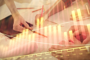 Double exposure of forex graph drawing and man and woman working together holding and using a mobile device. Trade concept.