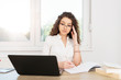 © Bojan Topalovic - Busy brunette in office wearing glasses, looking at laptop and writing on the paper.