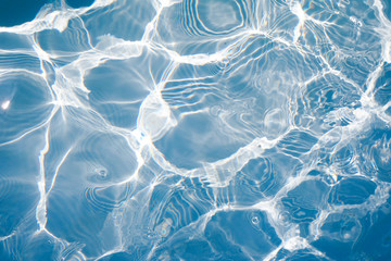 Blue water surface with bright sun light reflections, water in swimming pool background closeup