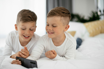 Two little brothers are playing games on the phone. Beautiful boys enjoying at home...