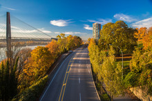 New Westminster City The Slopes Of The Fraser River, Painted With Autumn Colors, Sky Train Bridge And A Busy Road Against The Background Of A Bright Sky With White Clouds