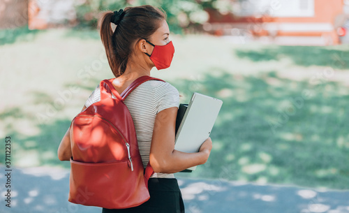 Fotomural Back to school university student girl wearing covid mask walking on campus with backpack, books and laptop