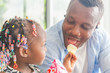 © JU.STOCKER - Cute little girl looking her dad eating snack, Cheerful african american father and daughter playing in living room, Happiness family concepts