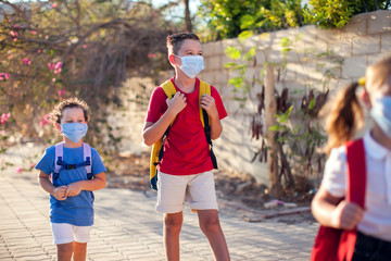 Wall Mural - Pupils with medical masks on face and backpacks going to school. Education during coronavirus time. Back to school.