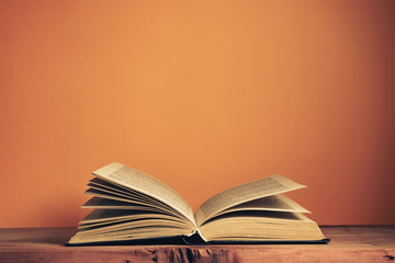 Poster - Old  open book on a oak wooden table. Background of orange wall behind.