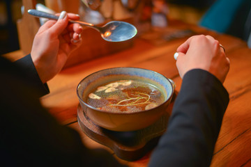 Young woman eating soup served in a white bowl. Eating out. Restaurant concept. Woman' s hand holding spoon.