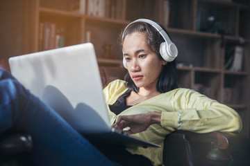 Wall Mural - Businesswoman working online at the home office via laptop. Asian young entrepreneur watching webinars and talking during meeting video conferences call with team. Woman sitting at sofa in living room