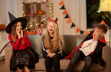 Sticker - halloween, holiday and childhood concept - smiling boy and girls in costumes playing and scaring each other at home at night