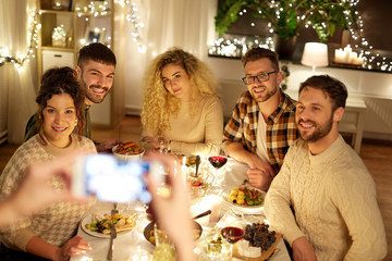 Wall Mural - holidays, celebration and people concept - happy friends being photographed with smartphone at home christmas dinner party