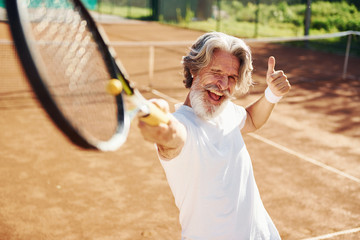 Playing game. Senior modern stylish man with racket outdoors on tennis court at daytime